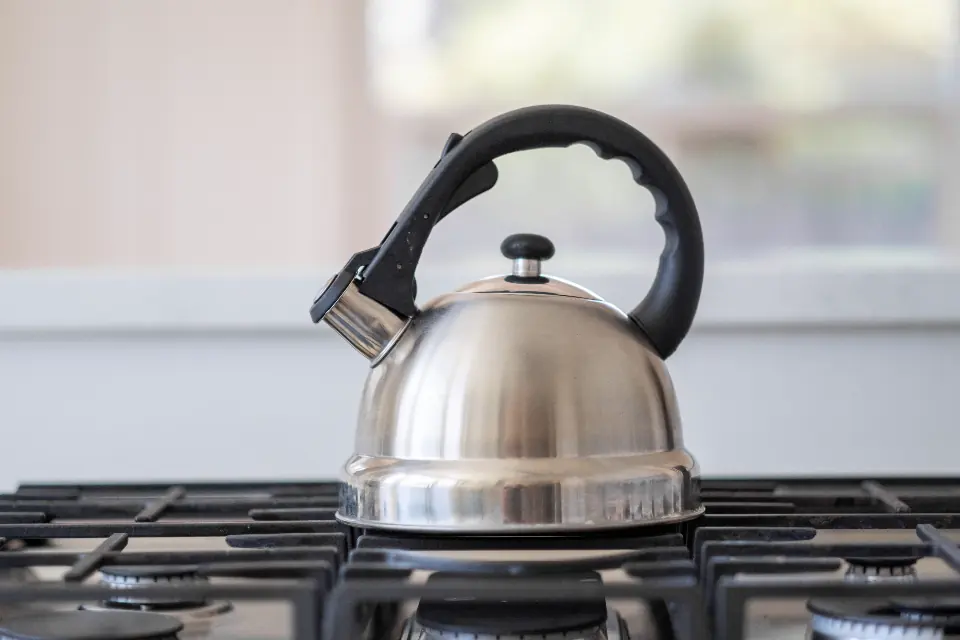 A steel kettle on a gas stove in a kitchen, the original photo.
